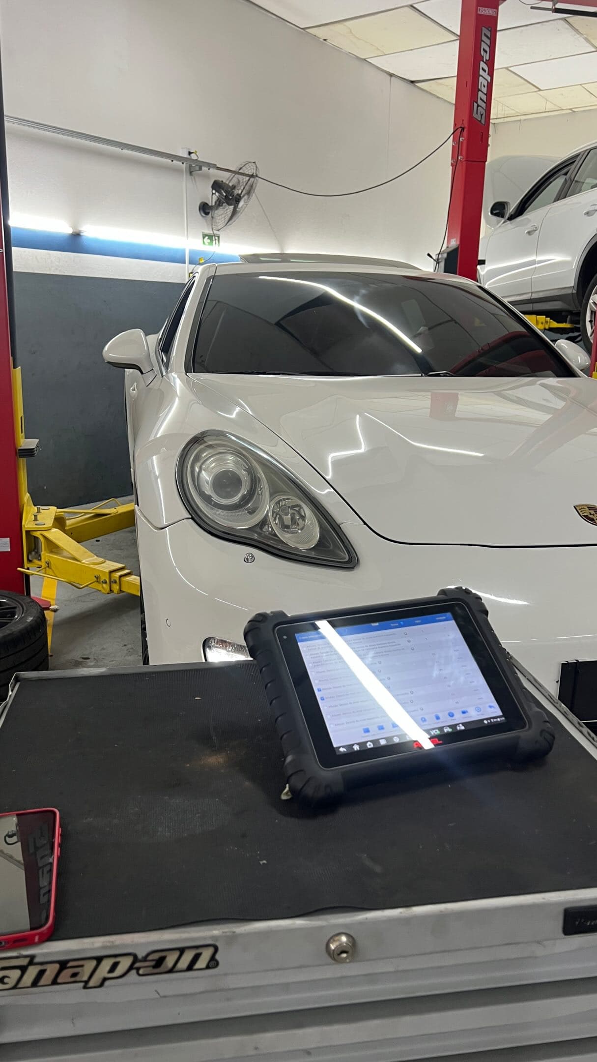 Scanner de diagnóstico sobre o carrinho Snap-on, em frente a um Porsche Panamera branco no salão da RCI